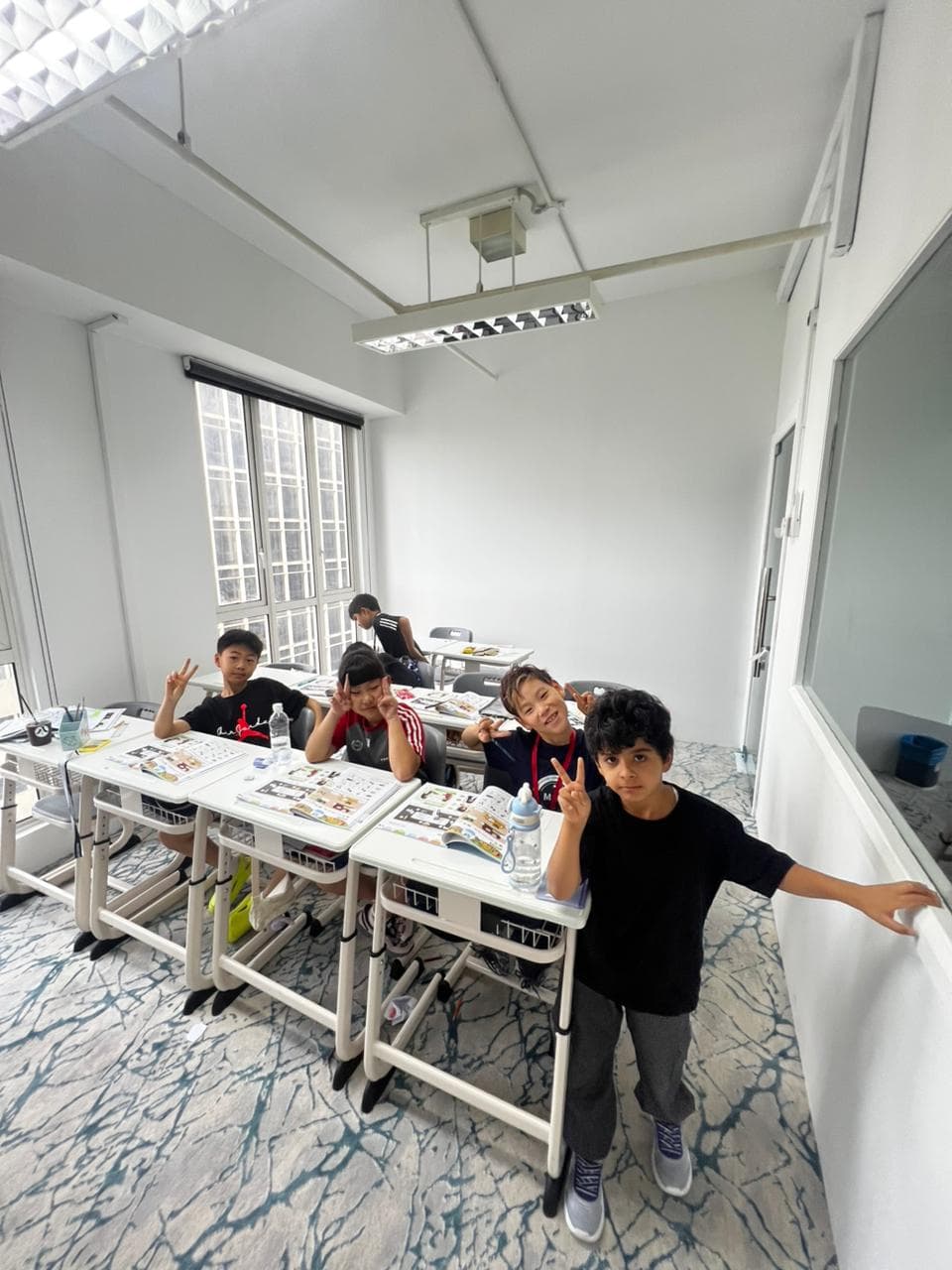 Four students at their desks in a bright classroom, mid-lesson
